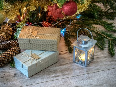 lit candle inside lantern beside gift boxes and christmas tree
