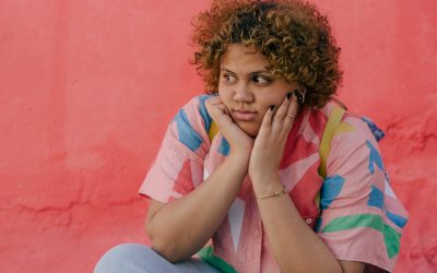 thoughtful young ethnic plump lady in colorful clothes sitting in street near pink wall