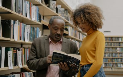 man in yellow sweater holding book beside woman in brown sweater